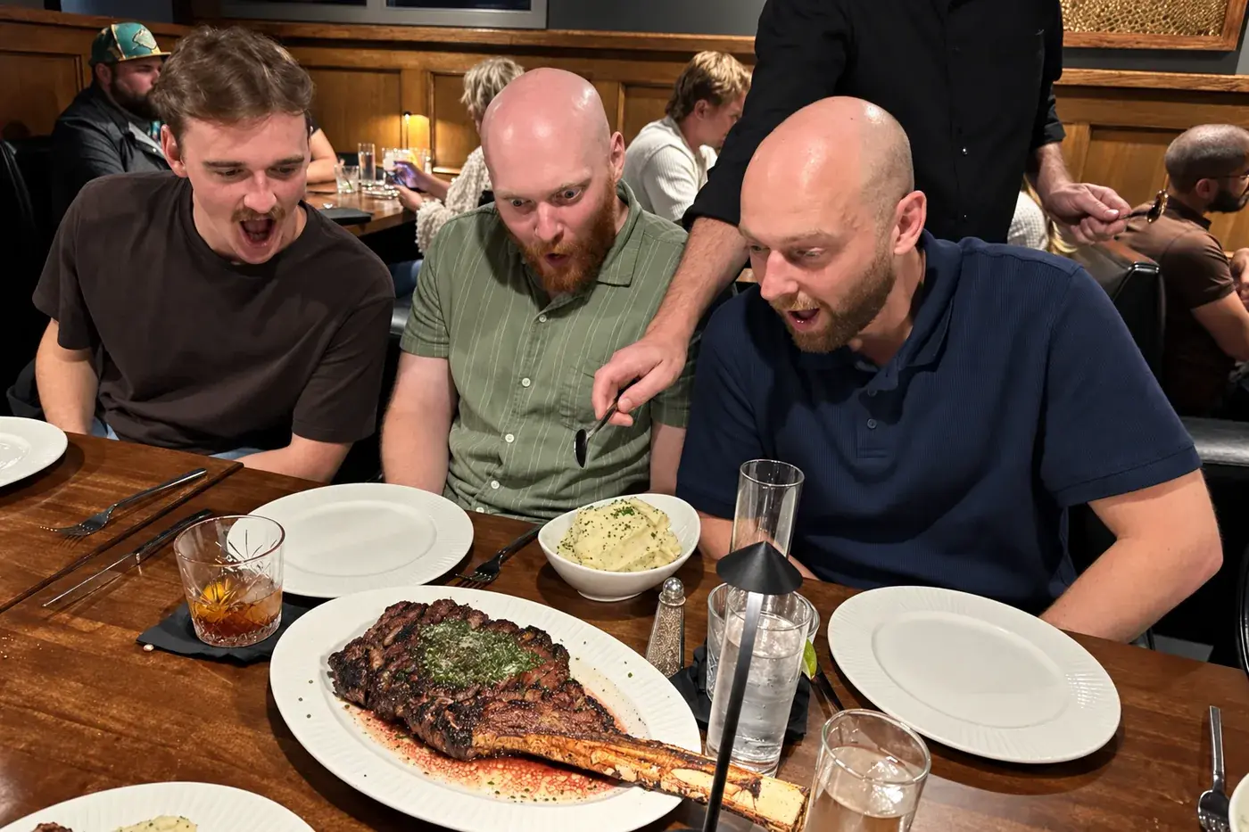 Tres del equipo inclinados sobre un corte tomahawk en la mesa de un restaurante.